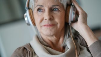 Senior woman at home listening to music with smartphone and headphones.