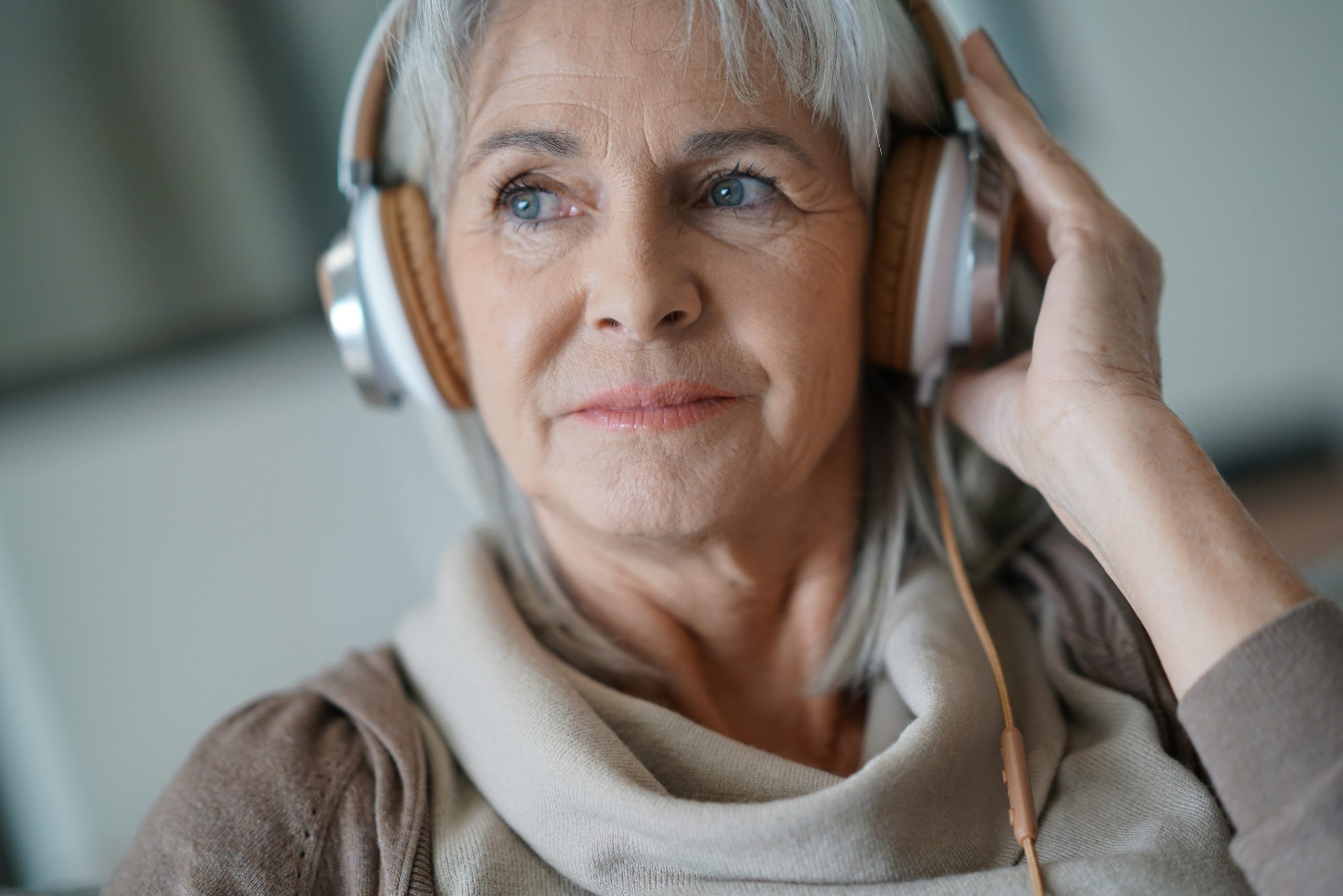 Senior woman at home listening to music with smartphone and headphones.