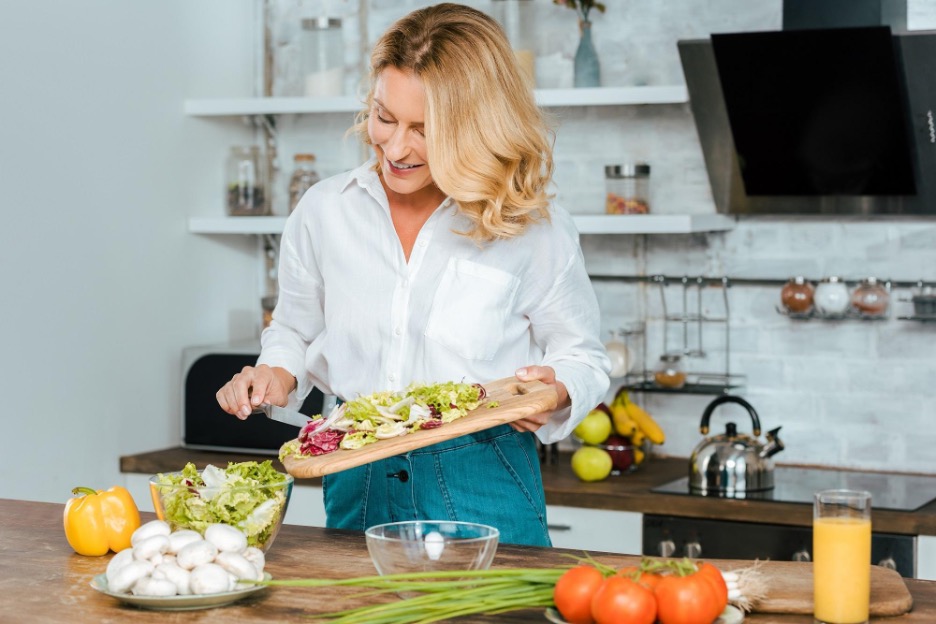 Woman adding chopped vegetables into salad.