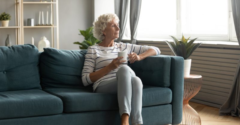 Older woman sitting on the blue sofa, holding a cup of coffee 