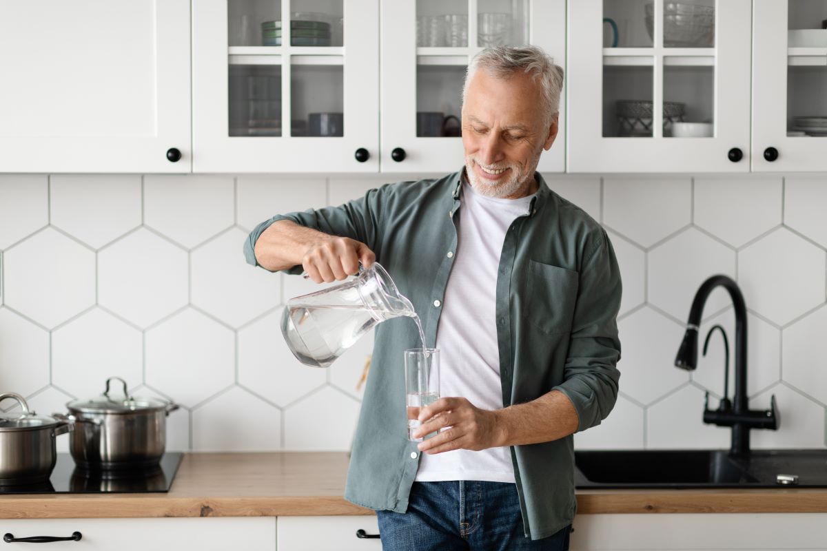 Handsome gray-haired man pouring water into a glass